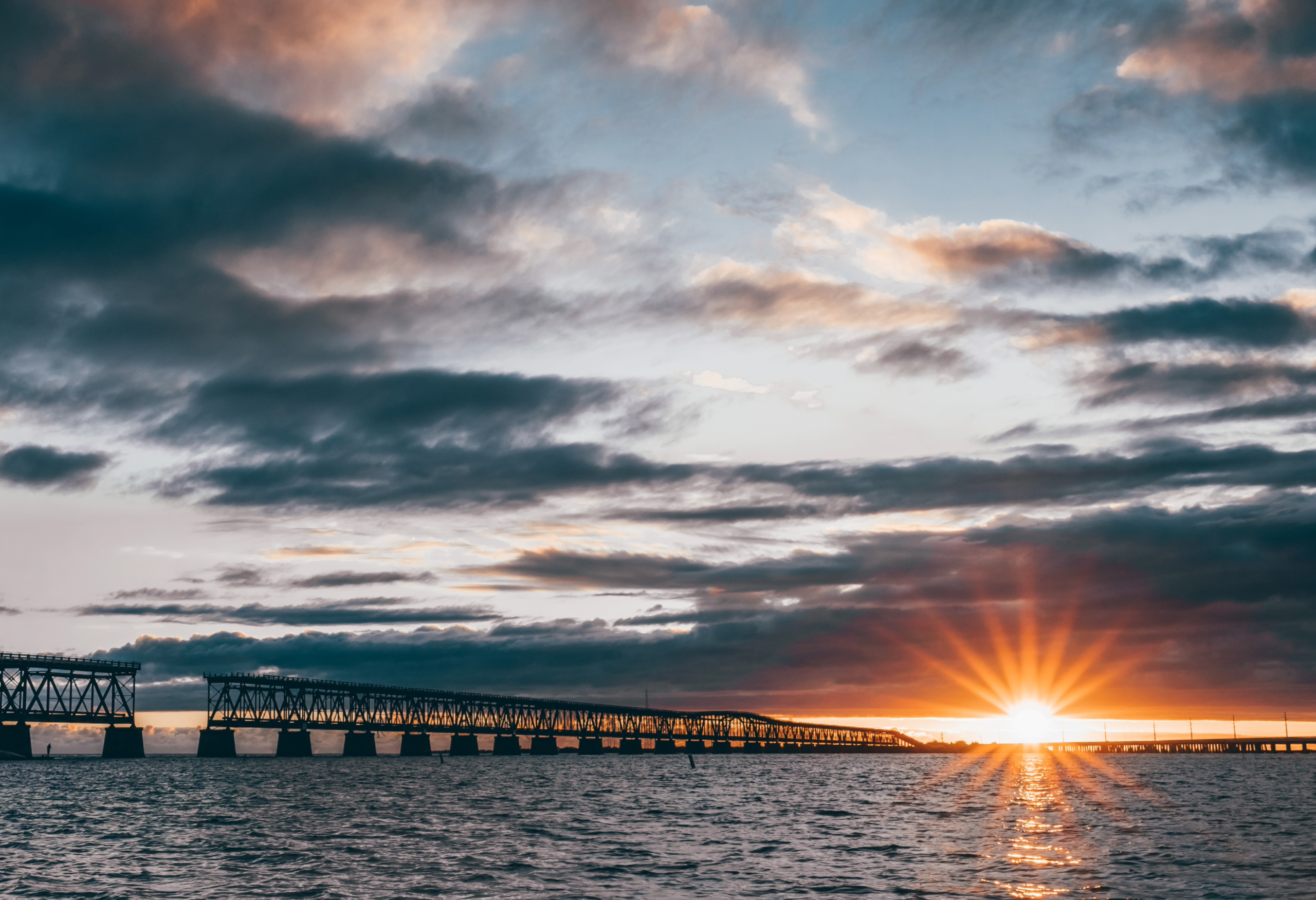 Sunset over a bridge and water with dramatic clouds.
