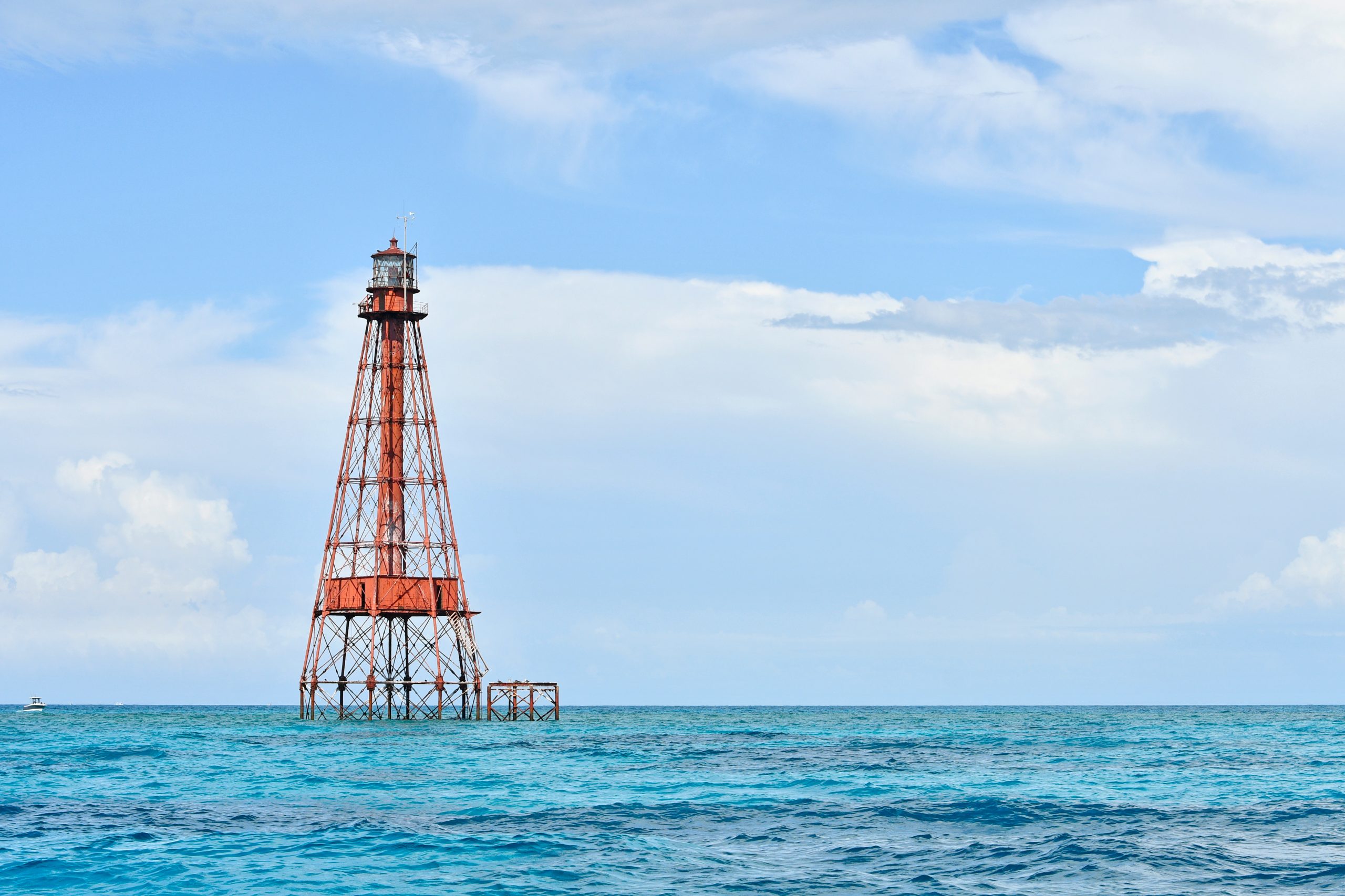 Red lighthouse on stilts in the ocean under a blue sky.